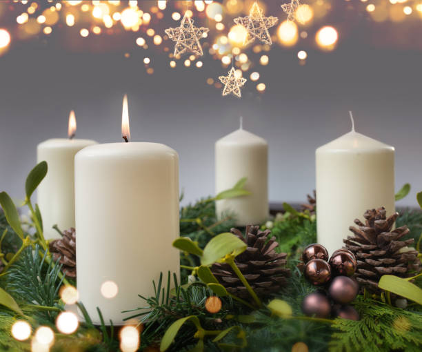 Two burning candle in a advent wreath of fir branches with christmas ornament and golden bokeh. Festive background with short depth of field for the christmas season with space for your text.